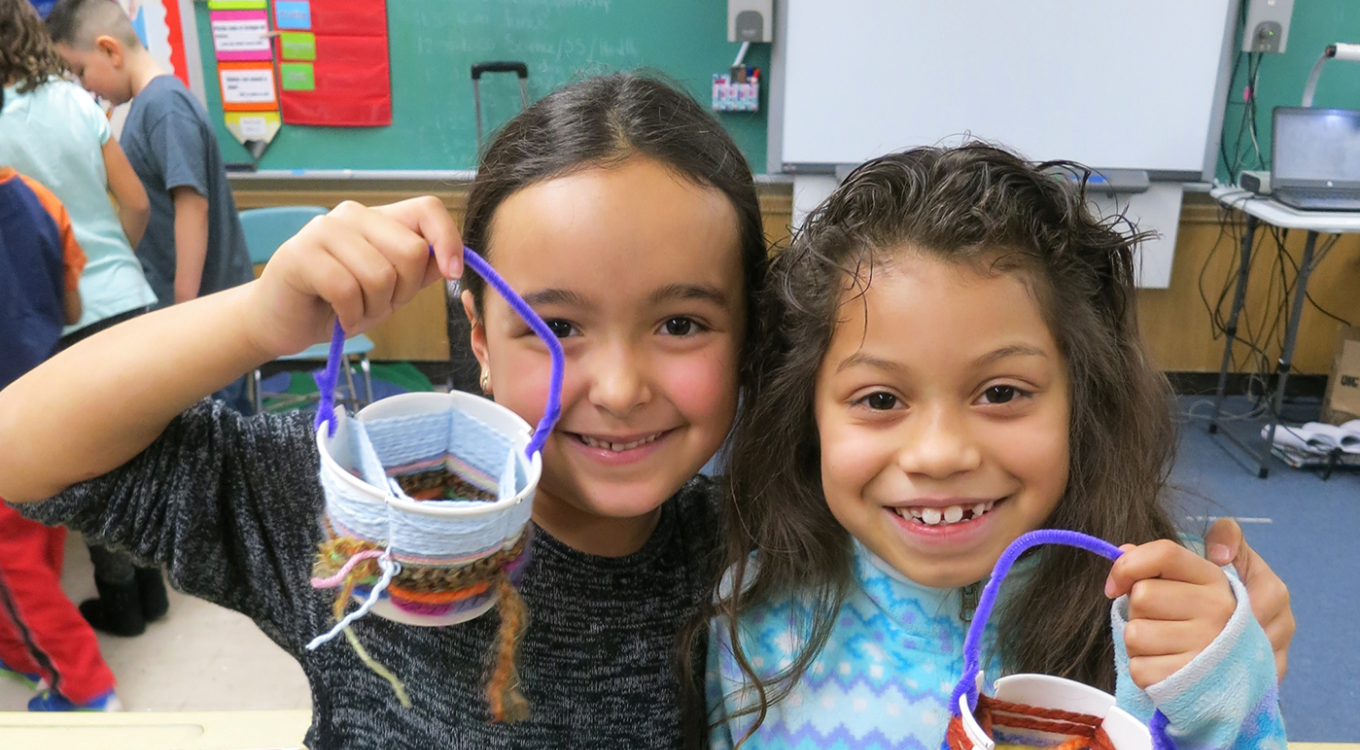 Two girls in classroom holding up handmade easter baskets