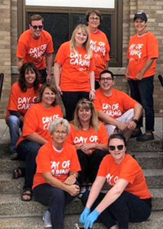 Andis Associates sitting on steps in orange shirts volunteering for Day of Caring