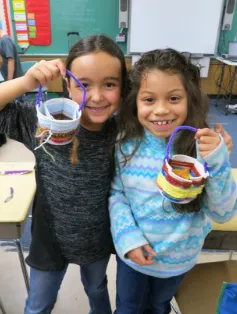 Two girls in a classroom holding up homemade easter baskets